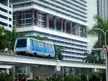 Miami metrorail automated people mover on an elevated track by a high-rise building with colorful pillars and palm trees