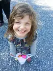 A smiling child with curly brown hair in a floral print dress holding a basket of colorful eggs