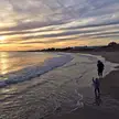 Two people walking along a sandy beach at sunset with gentle ocean waves