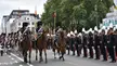 Soldiers in elaborate uniforms with tall hats on horseback and on foot parading through a city street