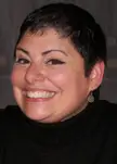 A smiling person with short dark hair wearing a black ribbed turtleneck sweater.