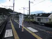 Nagasato Station platform with tracks, a small station building, and overhead power lines under a cloudy sky