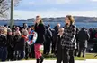 Bareneed and a group of people with a floral wreath by the water with hills in the background