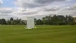 A white cricket sight screen on a green grass field at a Surrey County Cricket Club ground