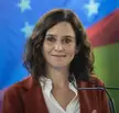 Isabel Díaz Ayuso with curly brown hair wearing a red blazer and white shirt against a colorful star backdrop