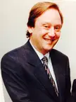 Charles Harnick smiling in a dark suit, white shirt, and patterned tie.