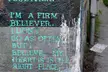 Tattoo design inspiration of teal text on a textured wall reading "I'M A FIRM BELIEVER... MY HEART IS IN THE RIGHT PLACE."