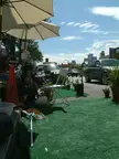 Group of people in casual clothing and baseball caps at an outdoor city street cafe with artificial grass and BMW cars
