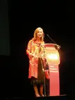 Blonde woman in a red jacket and black dress speaking at a podium for Unión Progreso y Democracia