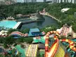 Aerial view of a water park with colorful water slides, a lagoon, and a volcano structure near a city skyline.