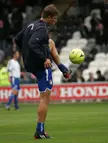 Paartalu in athletic wear kicking a yellow soccer ball on a grass field in front of stadium seating