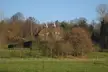 A brick house with pointed roofs in the rural countryside of Kent, surrounded by trees and a wooden fence.