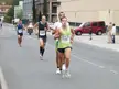 Four runners in athletic wear and tank tops racing on a road with motorcycles and cars in the background
