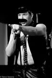 Accountants of Homeland Security RNC show 4: man in leather cap and vest with a fake mustache holding a microphone