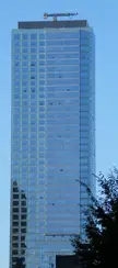 Tall modern glass skyscraper with a construction crane on its roof against a clear blue sky
