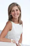 Businessperson with blonde hair and pale skin wearing a white tank top and hoop earrings, smiling.
