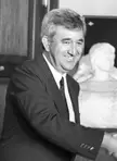 Gabriel Cañellas smiling in a dark suit and white shirt, black and white close-up with a statue in the background