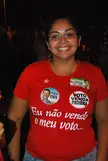 A smiling plus-size woman in a red t-shirt and blue denim jeans against a dark background.