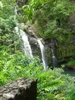 Waterfall on Road to Hana cascading down a rocky cliff with lush green tropical foliage and ferns.