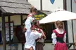 Group of people in Renaissance costumes with red dresses, white off-the-shoulder blouses, and brown trousers.