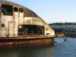 A rusted white structure resembling a torpedo or fuselage floating in water near a dock