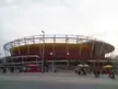 Olympic Tennis Center stadium with a red and yellow exterior and people in athletic wear walking in the plaza