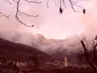 Samone, Trentino village at the base of snow-capped mountains under a pink sunset sky with bare tree branches