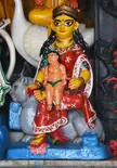 Shashthi statue of a woman in a red and green sari holding a child, seated on a grey animal