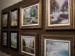 Eight framed fine art oil paintings of landscapes and architecture on a brown wall at the Plaza Gallery