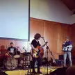 Metal dudes at the Mirah show featuring a guitarist, drummer, and singer on an indoor stage.