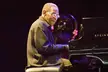 George Cables, a slender man with dark skin and glasses, looking down while playing a black Steinway piano.