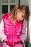 A blonde girl in a pink vest and plaid pants looking down, leaning against a white post at Walpack Center.