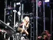 Kesha with blonde hair and a black dress performing on a concert stage with musicians