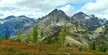 Mount Benzarino landscape with rugged rocky mountains, evergreen trees, and autumn foliage under a cloudy blue sky