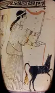 Artemis in a long pleated robe and headpiece pouring a libation from a bowl next to a black animal on ancient pottery.
