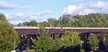 Continuous truss bridge crossing a lush green area with trees and street lamps in Kingston