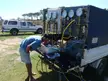 Man in a blue t-shirt, denim shorts, and baseball cap working on diving equipment in a white truck
