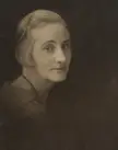 A vintage sepia-toned portrait of a woman with short wavy blonde hair, a black dress, and a beaded necklace.