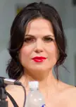 Lana Parrilla in a close-up with dark wavy hair, red lipstick, and an off-the-shoulder top.