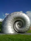The spire by Liz Lemon, a metallic spiral shell sculpture on a grassy field under a blue sky