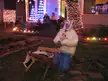 A person with a bag on their head and a figure on a lounge chair among Christmas lights and people on stairs
