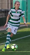 Blomquist, a blonde female soccer player in a green and white striped uniform, dribbles a ball on a grass field.