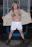 Man in a military helmet, bikini top, open tan jacket, white shorts, and black boots for an AVN Award for Best Actor