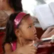 A petite Asian girl with a pink headband and white tank top sitting in a red seat on a river taxi in Bangkok.