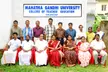 A group of people in white shirts, saris, and floral print dresses smiling in front of the University College of Teacher