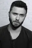 Stephen Sean Ford in a black and white close-up portrait with a beard and dark hair against a white brick wall