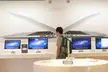 Man with a grey backpack and blue jeans standing before computer monitors and a giant laptop sculpture