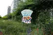 Welcome to Tsukiji sign with cartoon characters in a lush urban garden with flowers and buildings