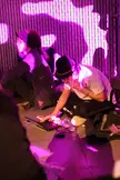 Two asian girls with pale skin and purple hair sitting in a room with purple lighting and projections