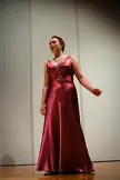 A curvy woman with reddish-brown hair wearing a shimmering magenta satin floor-length dress and a necklace.